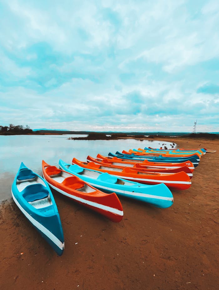 A vibrant arrangement of kayaks on a sandy beach under a cloudy sky.