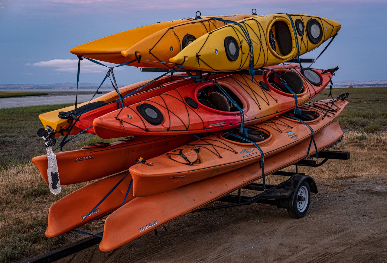 gallery-3 Colorful kayaks stacked on a trailer ready for adventure in a scenic outdoor setting.
