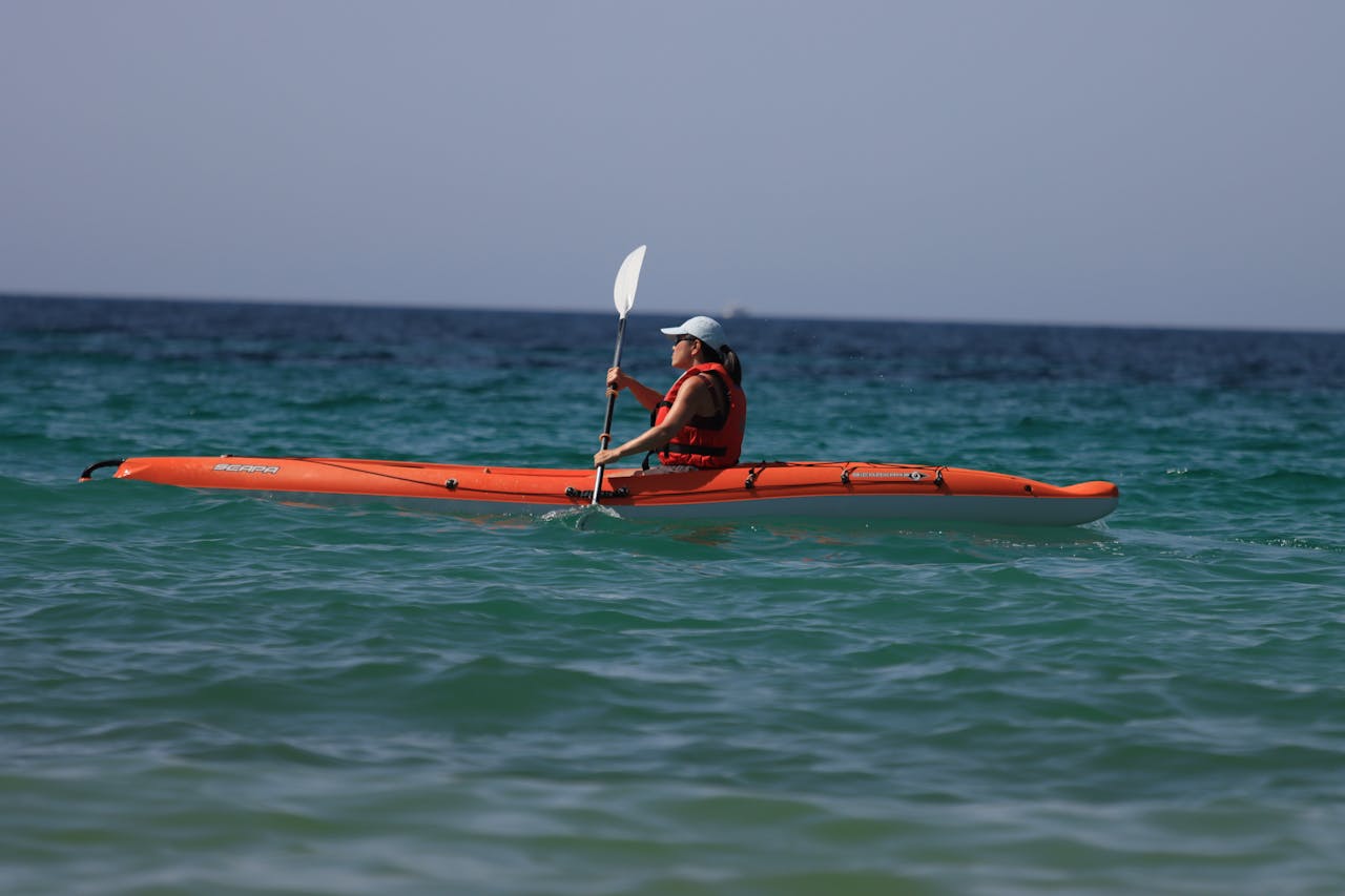 hero-img-02 Woman kayaking in vibrant orange kayak on open ocean on a sunny summer day.
