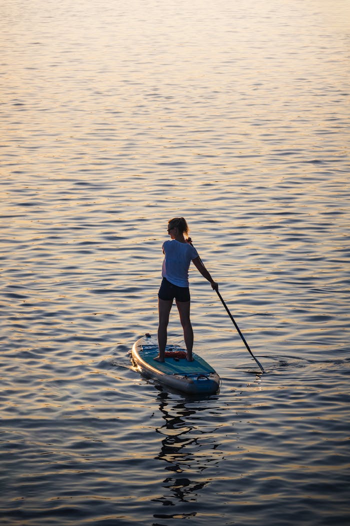 why-choose-us A woman enjoys stand-up paddleboarding on tranquil waters at sunset in Hamburg, Germany.