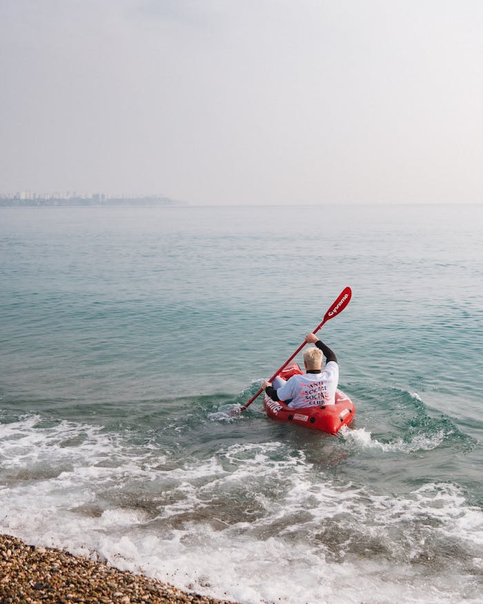services-01 A man kayaking on a serene sea near a pebble beach during summer, enjoying water sports and outdoor recreation.